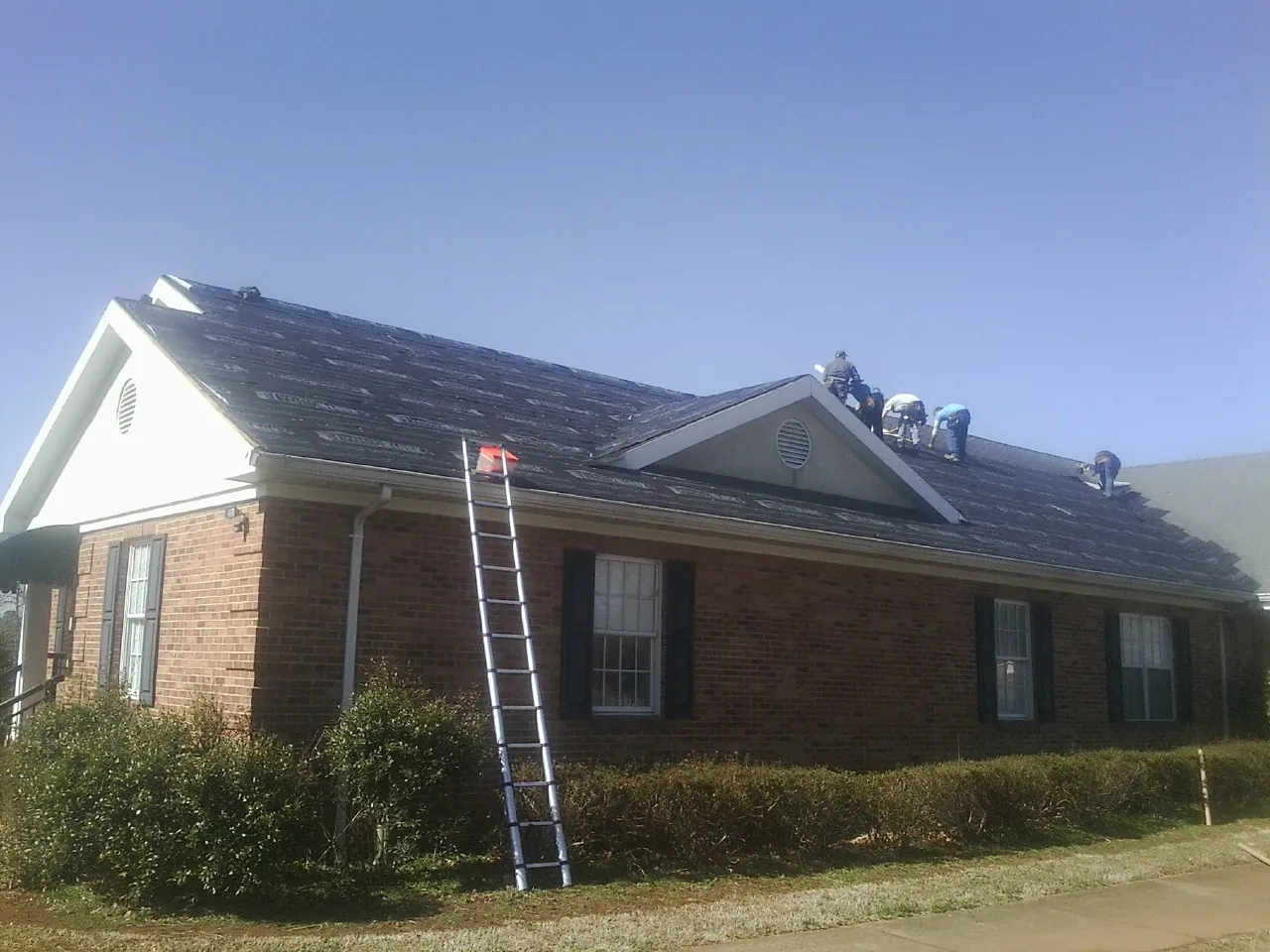 Crew tearing shingles off a brick ranch roof with a ladder set — Emergency Roof Repair work by our crew in Lockwood