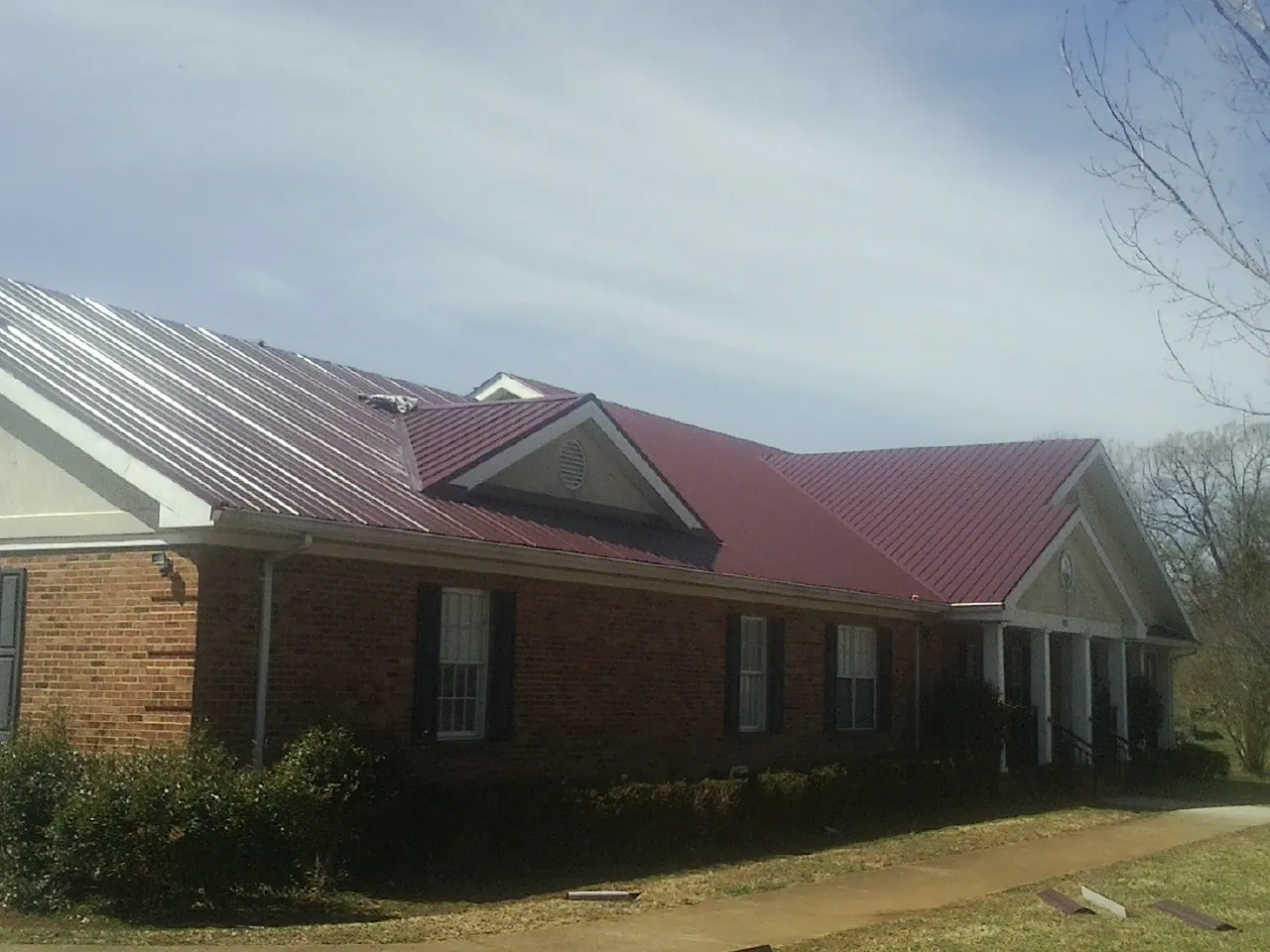 Red metal roof with gabled entries on a long brick building, from a Hail Damage Roof Repair job in Lockwood