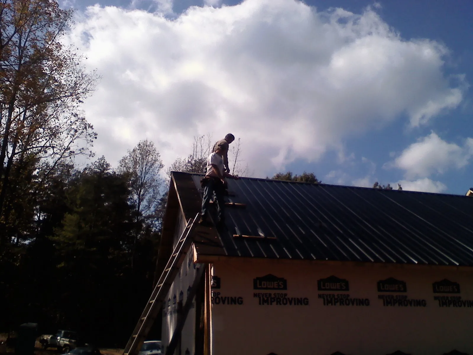 Roofer fastening dark metal panels high against a cloudy sky, from a Roof Inspection job in Lockwood