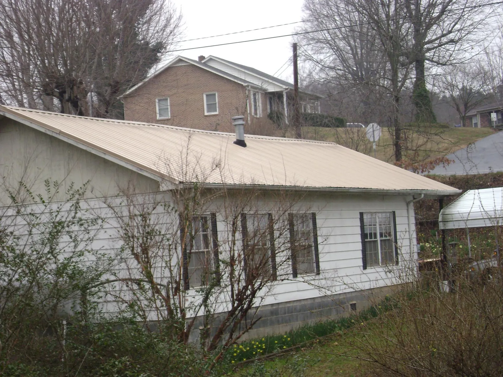 Tan metal roof on a white sided house set into a hillside — Commercial Roofing by Roofing Brothers in Lockwood